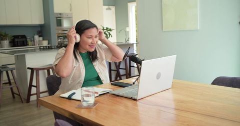 Mature woman podcasting from home office with laptop and microphone