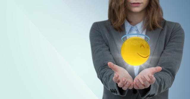 Business woman with hands out holding a glowing halo emoji representing positivity and integrity. Ideal for articles or campaigns focused on business ethics, positive workplace culture, or emotional intelligence in professional settings.
