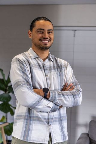 Confident asian man standing arms crossed smiling in office lounge with plaid shirt smartwatch
