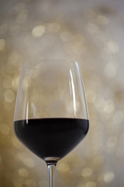 This image features a close-up of a red wine glass with a beautiful bokeh background, perfect for holiday and festive themes. Ideal for use in advertisements, blogs, or social media posts related to Christmas celebrations, elegant dining, or wine promotions.