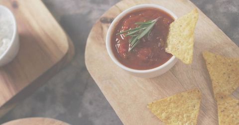 Rustic flatlay of chunky tomato salsa with rosemary and tortilla chips on wooden board