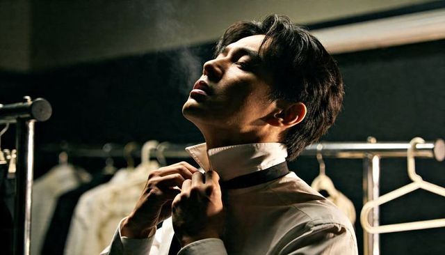 Backstage grooming man adjusting shirt collar and tie under cinematic low light atmosphere