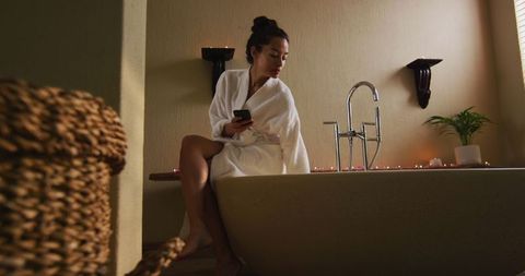 Serene moment in home spa, woman in robe using smartphone