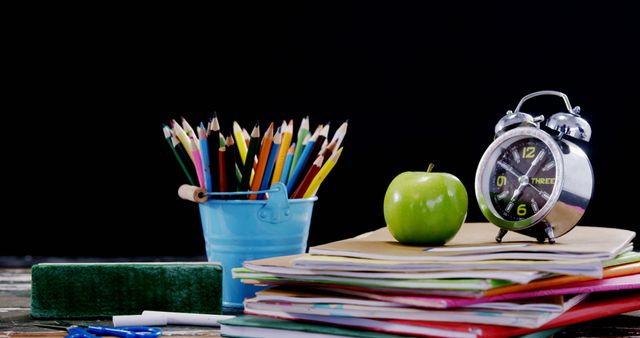 A collection of school supplies including colored pencils, books, and an alarm clock is arranged on a table, with copy space. These items symbolize the preparation and time management essential for academic success.