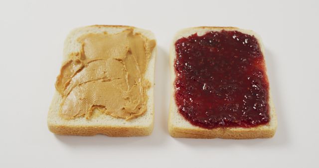 Peanut butter spread on one slice of white bread and jelly on another slice, ready to be combined into a peanut butter and jelly sandwich. Perfect for illustrating classic American snacks, lunch ideas, breakfast options, or simple meals.