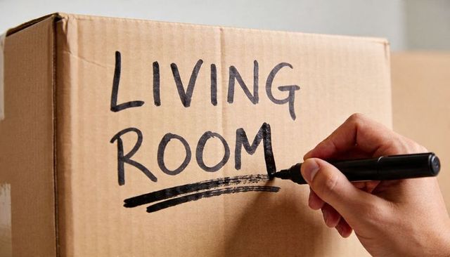 Labeling living room moving box with marker, close-up hand packing and organizing