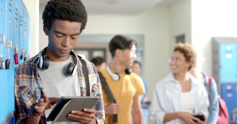 High School Student Using Tablet in Hallway with Friends Nearby