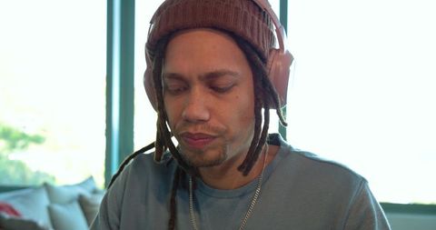 Man sitting by window wearing knit beanie and headphones, casual home workspace portrait