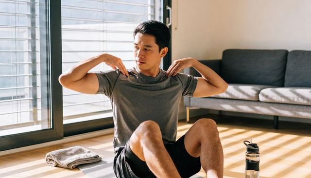 Sunlit home workout stretching man on mat by sliding doors with towel and water bottle