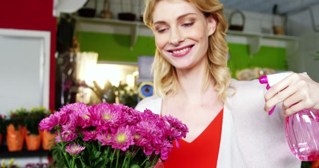 Woman florist spraying water on fresh pink flowers in a vibrant, modern flower shop. Ideal for content related to business, gardening, floristry, workplace happiness, flower care, and professional occupation.