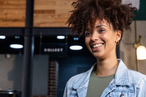 Young african american woman smiling and glancing at cafe pickup counter 'collect' sign