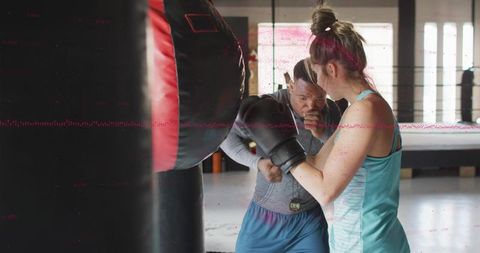 Trainer coaching female boxer on heavy bag in bright boxing gym