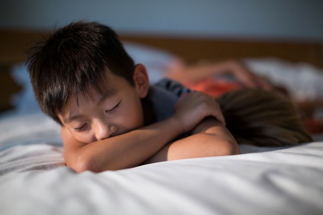 Young boy sleeping peacefully on a bed in a cozy bedroom at home. Ideal for use in articles or advertisements related to children's sleep, parenting, home life, or relaxation. Can also be used in educational materials about the importance of sleep for children.