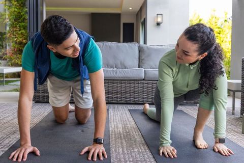 Couple practicing low-lunge yoga stretch on covered patio with mats and smartwatch