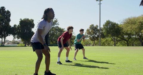 Diverse team warming up on grassy field catching ball in outdoor fitness training