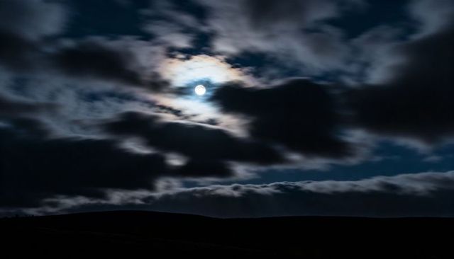 Shining Full Moon Casting Halo Over Rolling Hills Under Dramatic Cloudscape