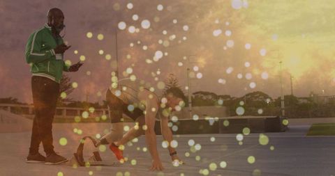 Sprinter preparing at starting blocks with coach on sunset track training session