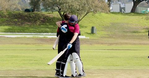 Two cricketers embracing on field displaying team spirit