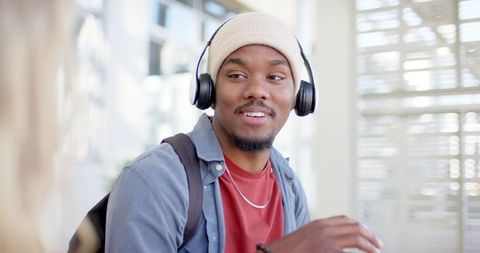 Smiling african american student wearing headphones and beanie in sunlit cafe