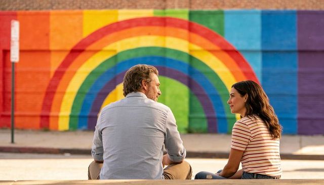 Couple Sitting on Curb Sharing Conversation in Front of Colorful Rainbow Mural