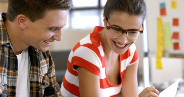 Two coworkers are sharing a joyful moment during a break in a creative office. The image can be used for websites and promotional materials related to positive work environments, teamwork, collaboration, and workplace culture. Ideal for illustrating articles about modern office life, team bonding, and employee engagement.