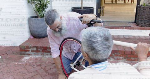 Mature couple repairing bicycle wheel on brick porch, diy teamwork and home maintenance