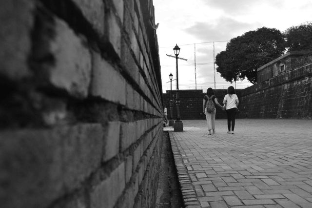 Two people walking hand in hand along a historic brick wall, great for themes of companionship, exploring urban settings, and casual strolls. Use for travel blogs, romance stories, or historic site promotions.