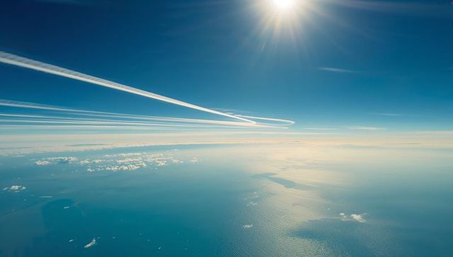 Contrails looping across deep-blue sky over sunlit ocean horizon with scattered clouds and islands