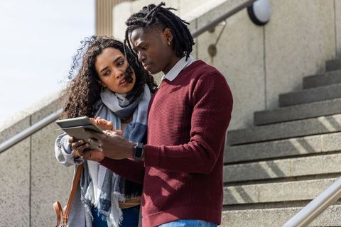 Young couple reviewing directions on tablet outdoors on urban stone steps, technology lifestyle