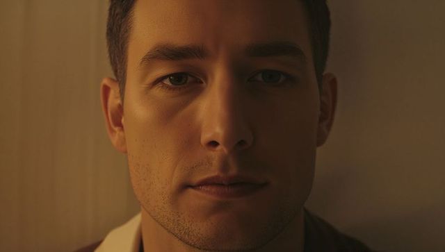 Warm low-key male headshot with calm gaze, centered composition, textured beige background