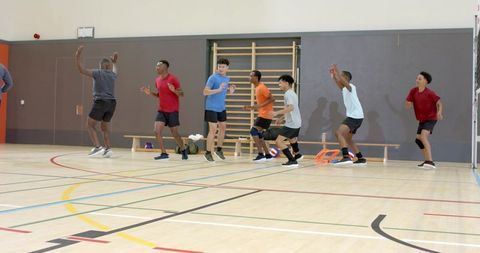 Youth male volleyball team training and jumping together during indoor gym warmup drill