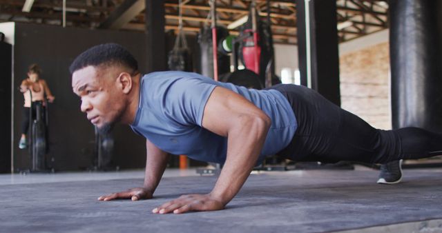 Man doing push-ups in modern gym, emphasizing physical fitness and determination. Use this image to promote healthy lifestyles, fitness programs, workout routines, or gym memberships.