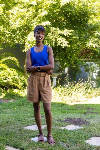 African american woman standing in sunlit backyard wearing smartwatch and belted shorts