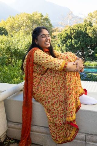 Joyful Indian Woman in Yellow Kurta Sitting Outdoors on Terrace