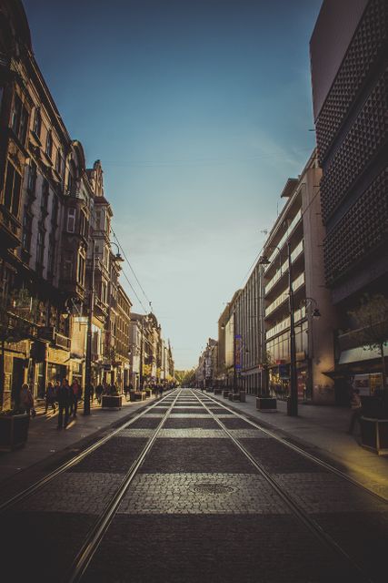 This photo captures an empty city street at sunset, featuring tram tracks and urban architecture. Use this image for city or transportation-themed projects, urban planning presentations, or articles related to travel and tourism.