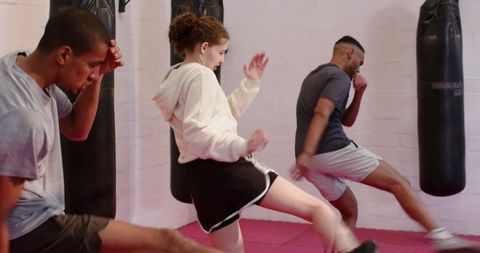 Teen girl performing front kick in kickboxing class with heavy bags, group training