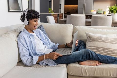 Young Man Relaxing on Sofa Using Laptop and Headphones at Home