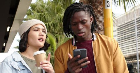 Young Couple Checking Phone at Bus Stop Holding Coffee Looking Concerned Urban Transit