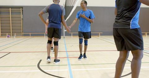 Diverse male volleyball players shaking hands showing sportsmanship on indoor gym court