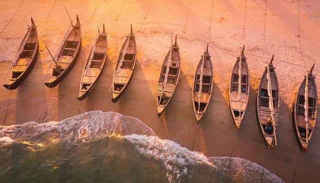 Golden sunset lined wooden fishing boats casting long diagonal shadows on sandy shoreline
