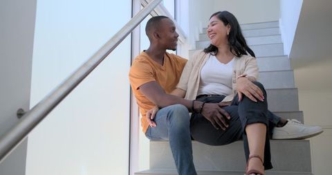 Young couple laughing and sharing intimate moment on modern staircase with frosted glass