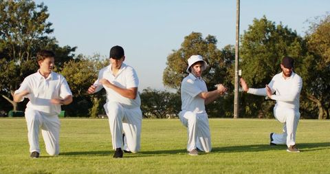 Four cricketers kneeling doing arm drills during outdoor training session