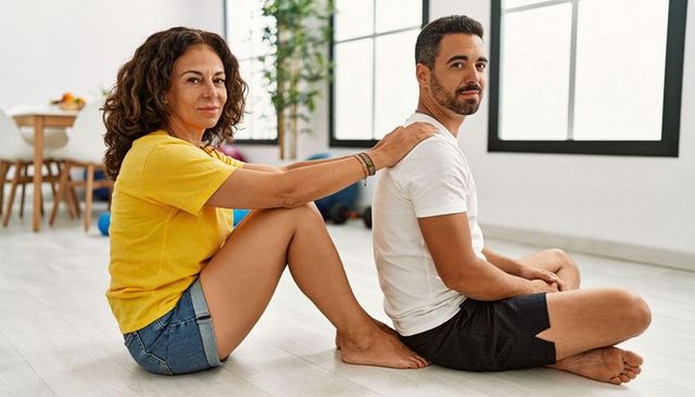Couple practicing partner shoulder massage and gentle stretching on sunny living room floor