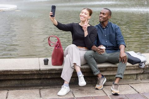 Young couple taking selfie by city fountain while enjoying coffee and casual afternoon