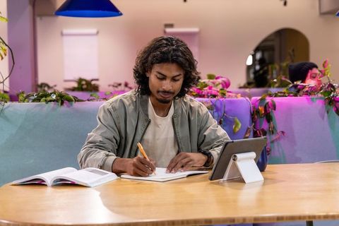 Focused young man studying with notebook and tablet in modern cozy coworking space