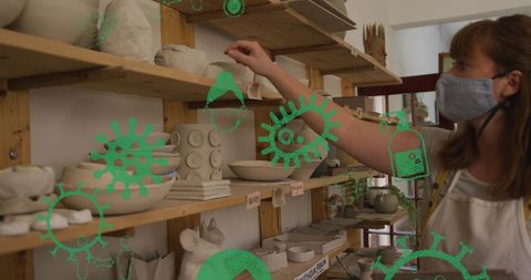 Masked woman observing pottery with digital virus icons overlay