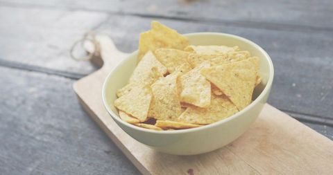 Green bowl holding golden tortilla chips on rustic cutting board, minimalist snack