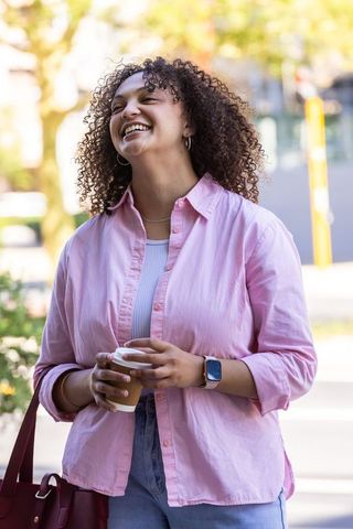 Young african american woman laughing holding takeaway coffee on sunlit urban sidewalk