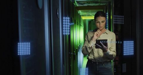 Female it engineer monitoring servers with tablet in datacenter aisle wearing beige shirt