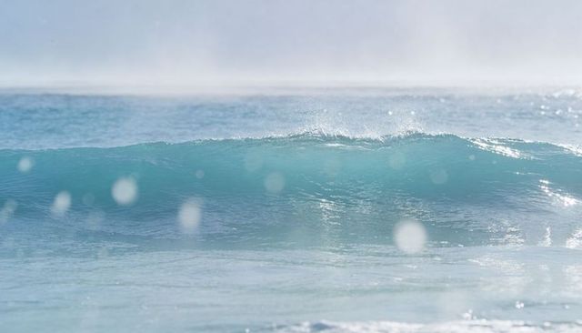 Turquoise wave rolling toward shore with foamy crest, sparkling bokeh and sea spray